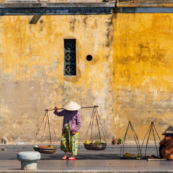 Vendeuse ambulante au chapeau conique devant un mur jaune, Hoi An, Vietnam